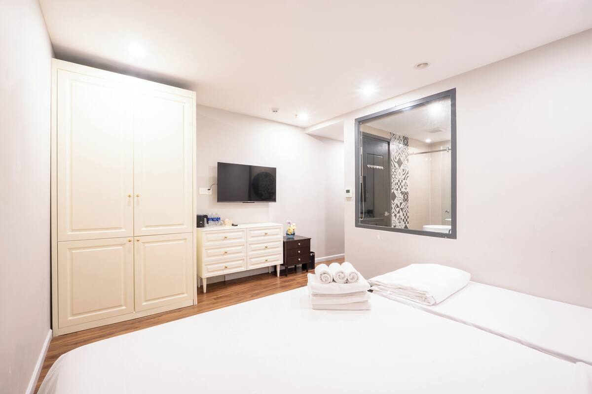 A bedroom with a large bed, a wardrobe, a dresser, a TV, and a bathroom with a shower and a mirror.