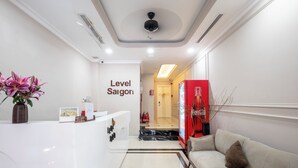 A reception area with a white reception desk, a sign reading "Level Saigon," a red Coca-Cola refrigerator, a beige sofa, and a vase with pink lilies. - Level Saigon hotel (Ho Chi Minh City)