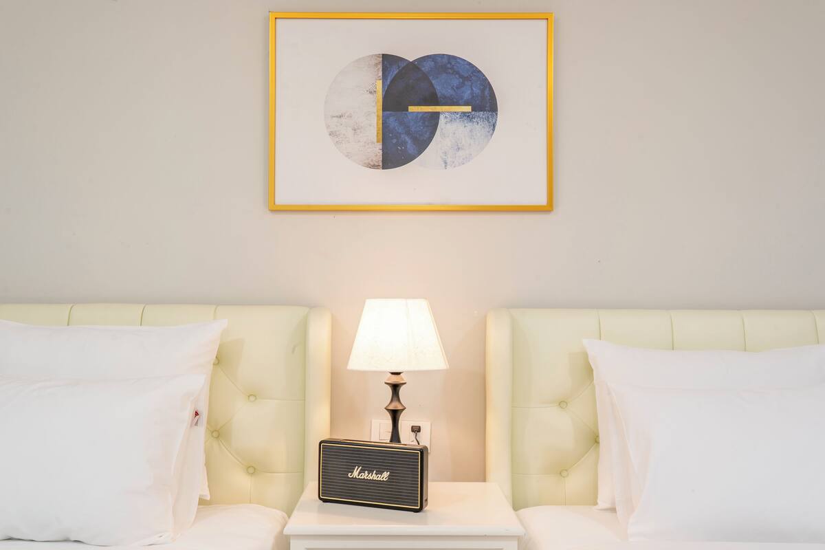A hotel room with a framed abstract artwork, a bedside lamp, a Marshall radio, and tufted headboards.