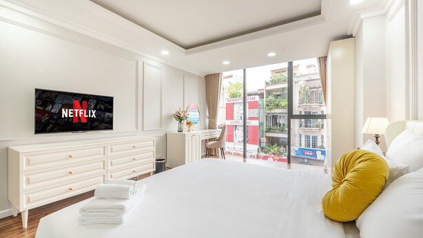 A hotel room with a large bed, a television displaying the Netflix logo, a desk with a chair, and a window with a view of the city. - Level Saigon hotel (Ho Chi Minh City)