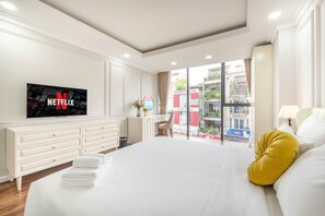 Una habitación de hotel con una cama grande, un televisor mostrando el logotipo de Netflix, un escritorio con una silla y una ventana con vista a la ciudad.
