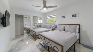 A bedroom with two beds, a ceiling fan, a TV, and a window with blinds.