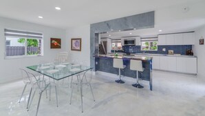 A modern kitchen with a glass dining table and chairs, white cabinets, and a blue backsplash.