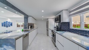 A modern kitchen with white cabinets, a marble countertop, a built-in oven, and a microwave.
