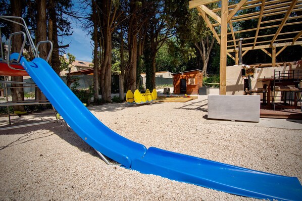 Un parque infantil con un tobogán azul, pelotas de seguridad amarillas y una estructura de madera.