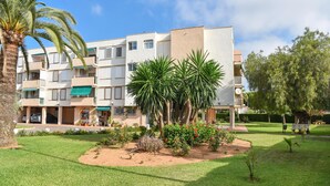 A multi-story residential building with balconies, a well-maintained lawn, and palm trees.