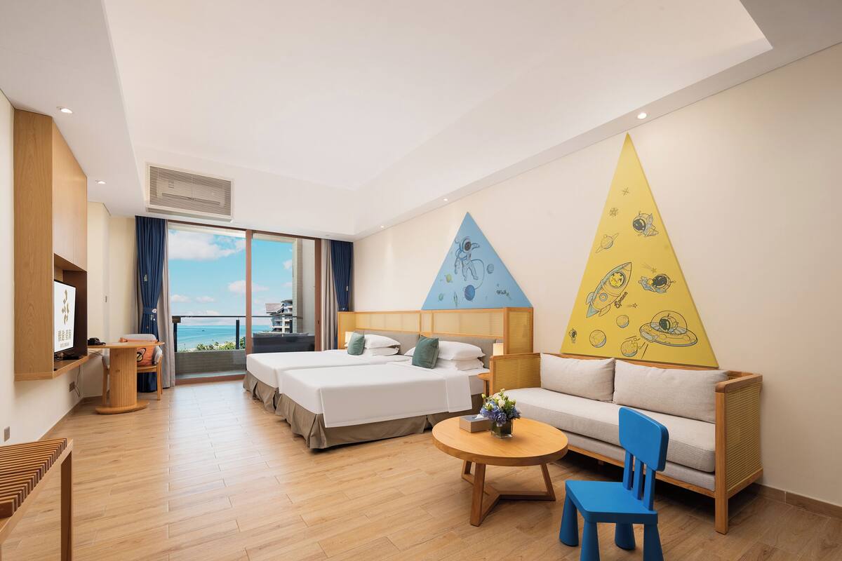 Habitació d'hotel amb dos llits, un sofà, una taula petita i una cadira. Hi ha una finestra gran amb vista al mar.