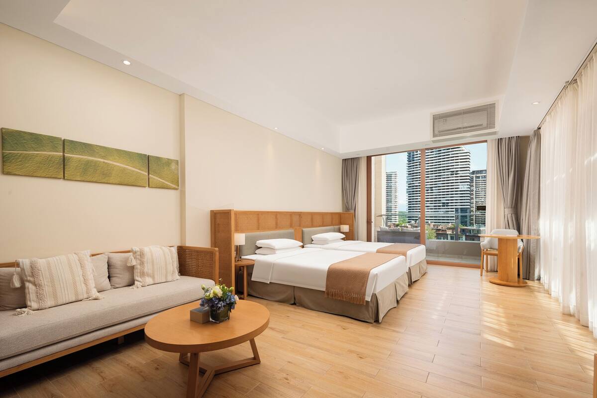Habitació d'hotel amb un sofà, dos llits, una taula rodona i vista a una ciutat.