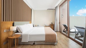 A modern hotel room with a large bed, a bedside table with a lamp, a small round table, and a chair. There is a sliding glass door leading to a balcony with outdoor seating. - Artel Shanwei - Xinghai Resort (Shanwei)