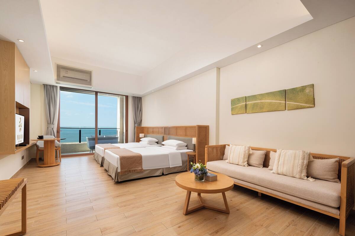 Habitació d'hotel moderna amb un llit gran, un sofà, una televisió i un balcó amb vista al mar.