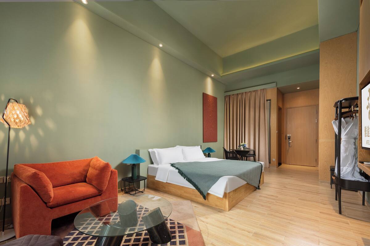 Una habitació d'hotel moderna amb un llit, un butàc armchair vermell, una taula de vidre i un escriptori amb una cadira.