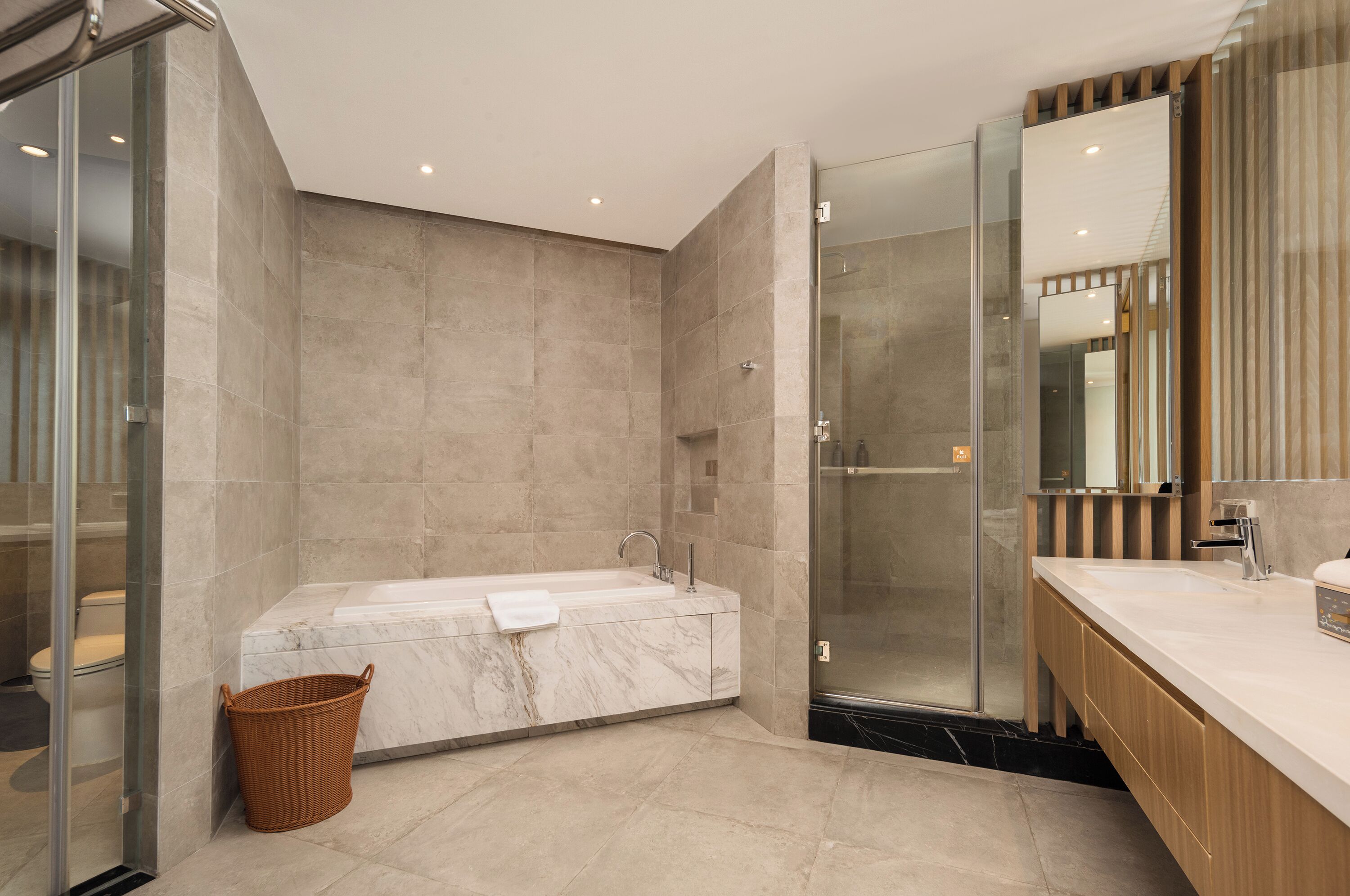 Un baño moderno con una bañera de mármol, una ducha con mampara de vidrio y un tocador de madera con espejo.