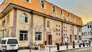 A hotel with a yellow facade, multiple windows, and a sign that reads "QAMAR HOTEL".