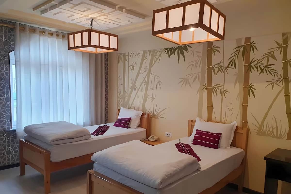 Una camera d'albergo con due letti in legno, una parete a tema bamboo, un soffitto con motivi geometrici e un lampadario.