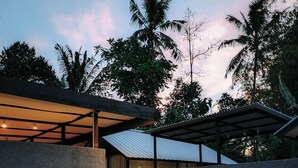 Una casa moderna con un porche cubierto, dos bicicletas y un jardín con plantas tropicales.