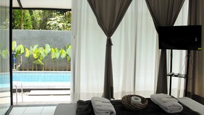 Habitación de hotel con cama, televisor, vista a una piscina y cortinas.