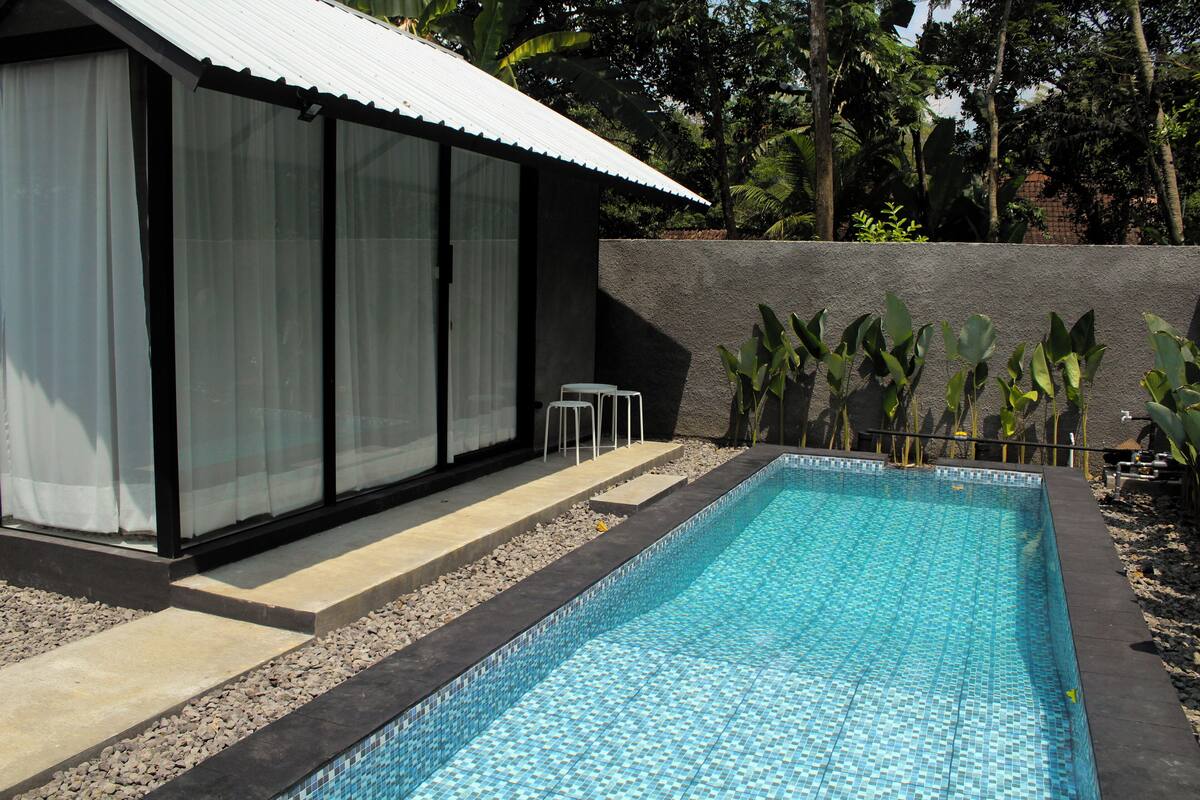 A swimming pool with a tiled edge, a covered seating area, and a building with large windows.