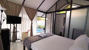 Habitación de hotel con cama, televisión, escritorio y vista a una piscina al aire libre.
