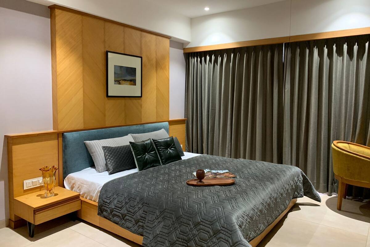 Un dormitorio moderno con una cama grande, una mesita de noche, una silla y una ventana con cortinas.