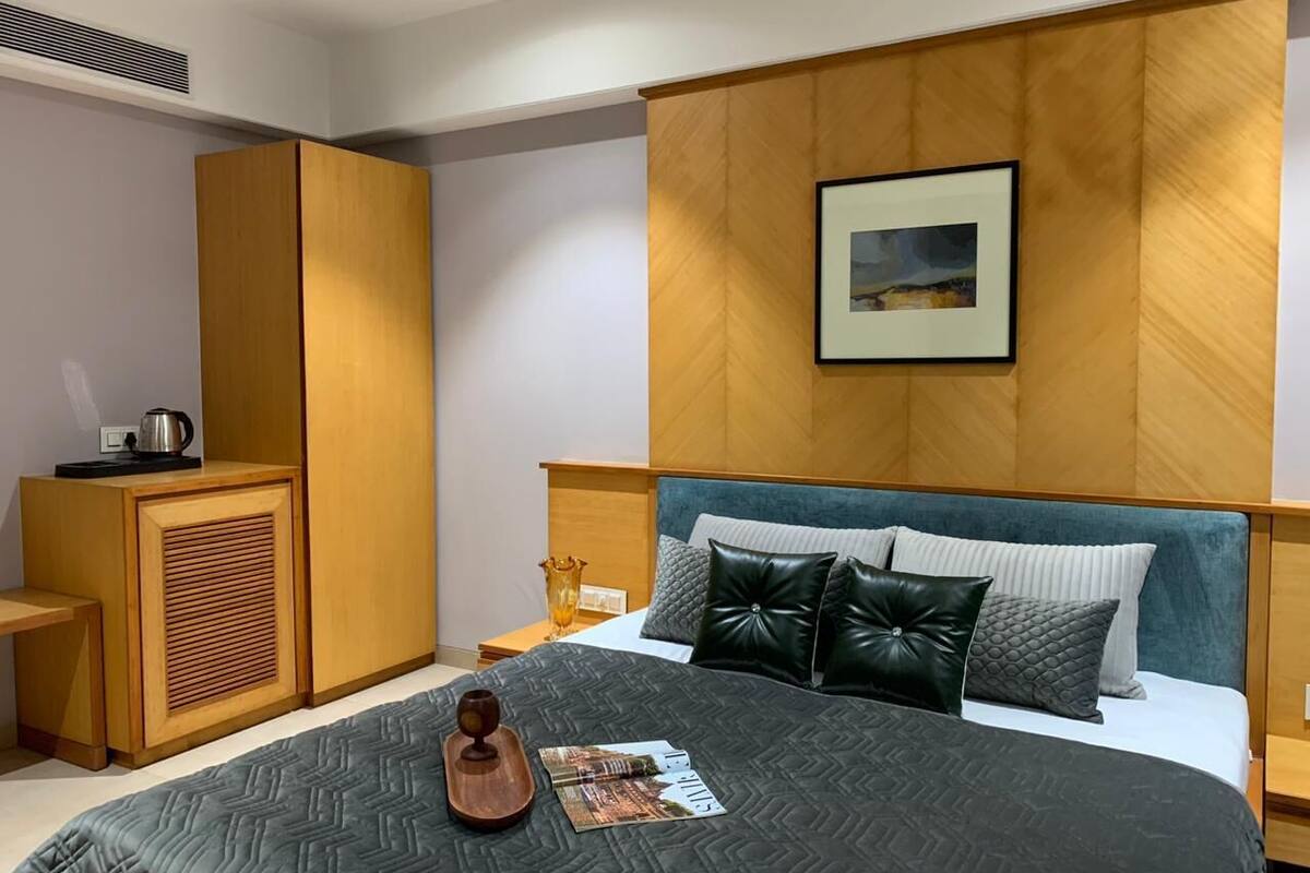 Una habitación de hotel moderna con una cama grande, un armario de madera y una mesita con una tetera.