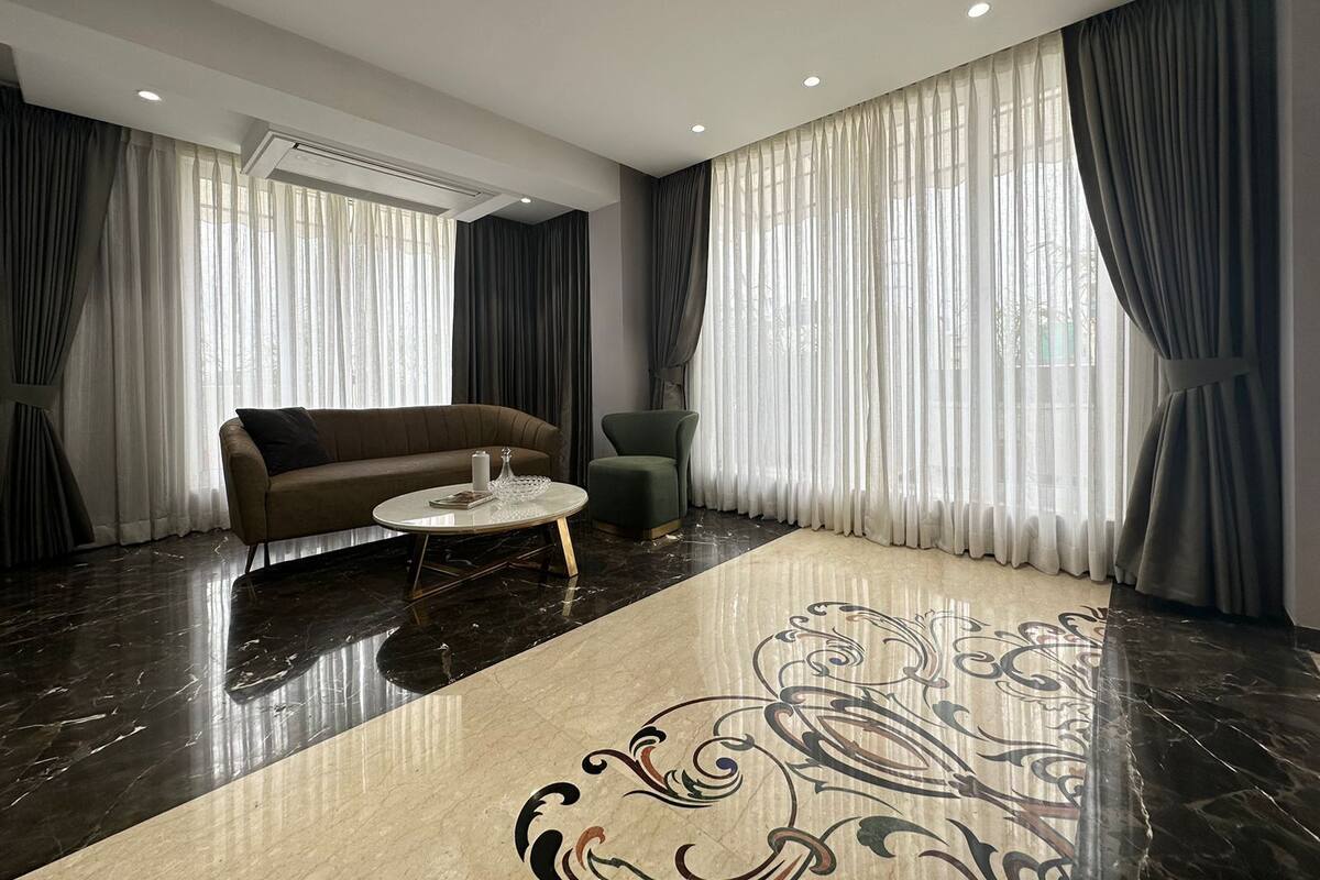 Un salón moderno con piso de mármol oscuro, un sofá marrón, un sillón verde y una mesa de centro redonda.