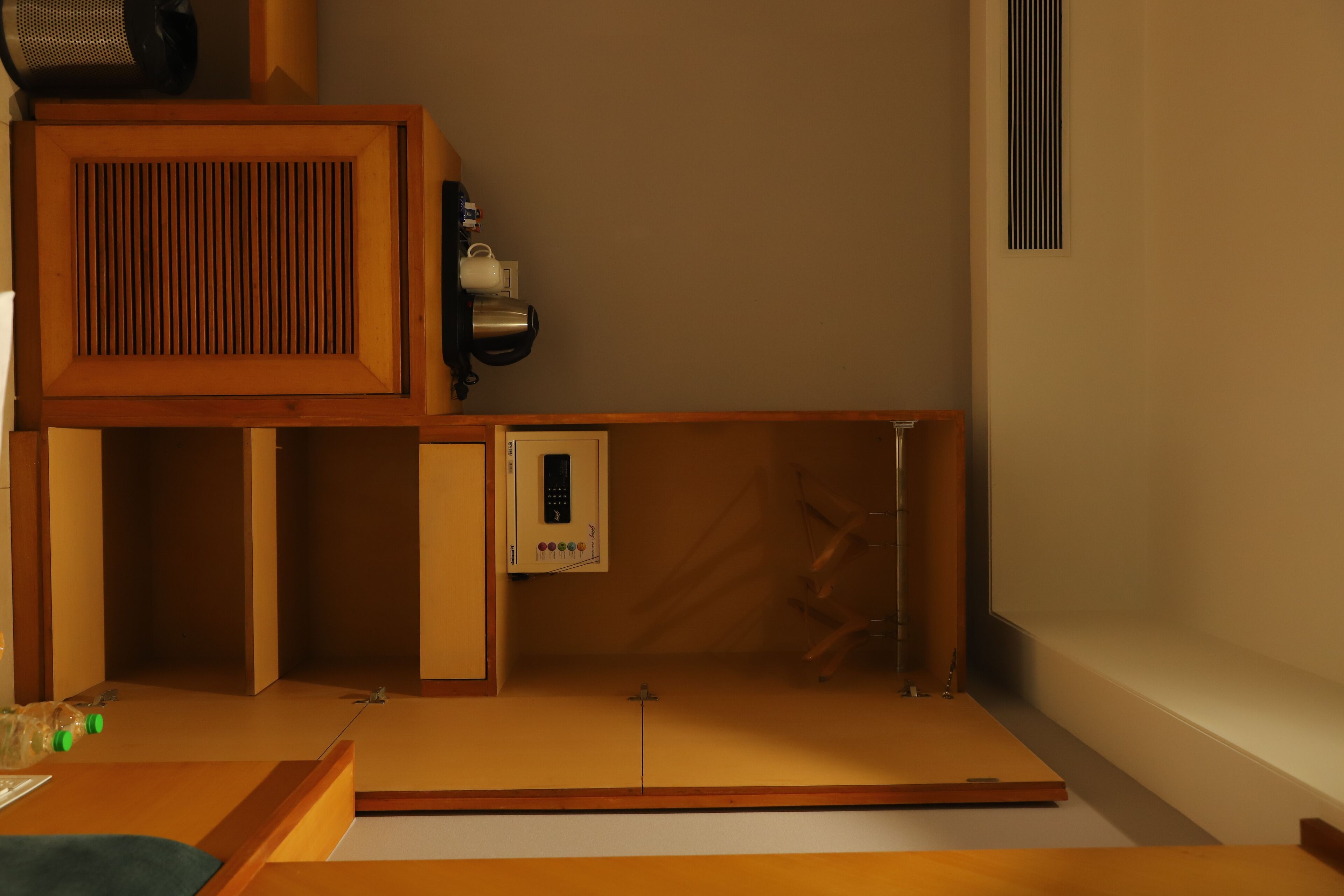 A room with a wooden cabinet, a small shelf with a kettle, a remote control, and a decorative item on the wall.