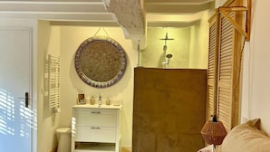 A bedroom with a bed, a bedside table, a mirror, a wall-mounted light fixture, and a wooden door. - Le Mas Brantôme (Brantôme en Périgord)