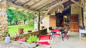 A rustic outdoor dining area with stone walls, wooden beams, and potted plants. - Le Mas Brantôme (Brantôme en Périgord)