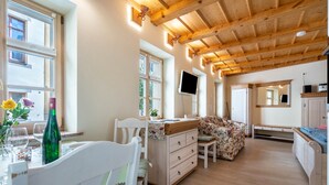 Une pièce avec un plafond en bois, une table à manger avec des chaises, un canapé à motifs floraux, un téléviseur fixé au mur et une fenêtre donnant sur des arbres.