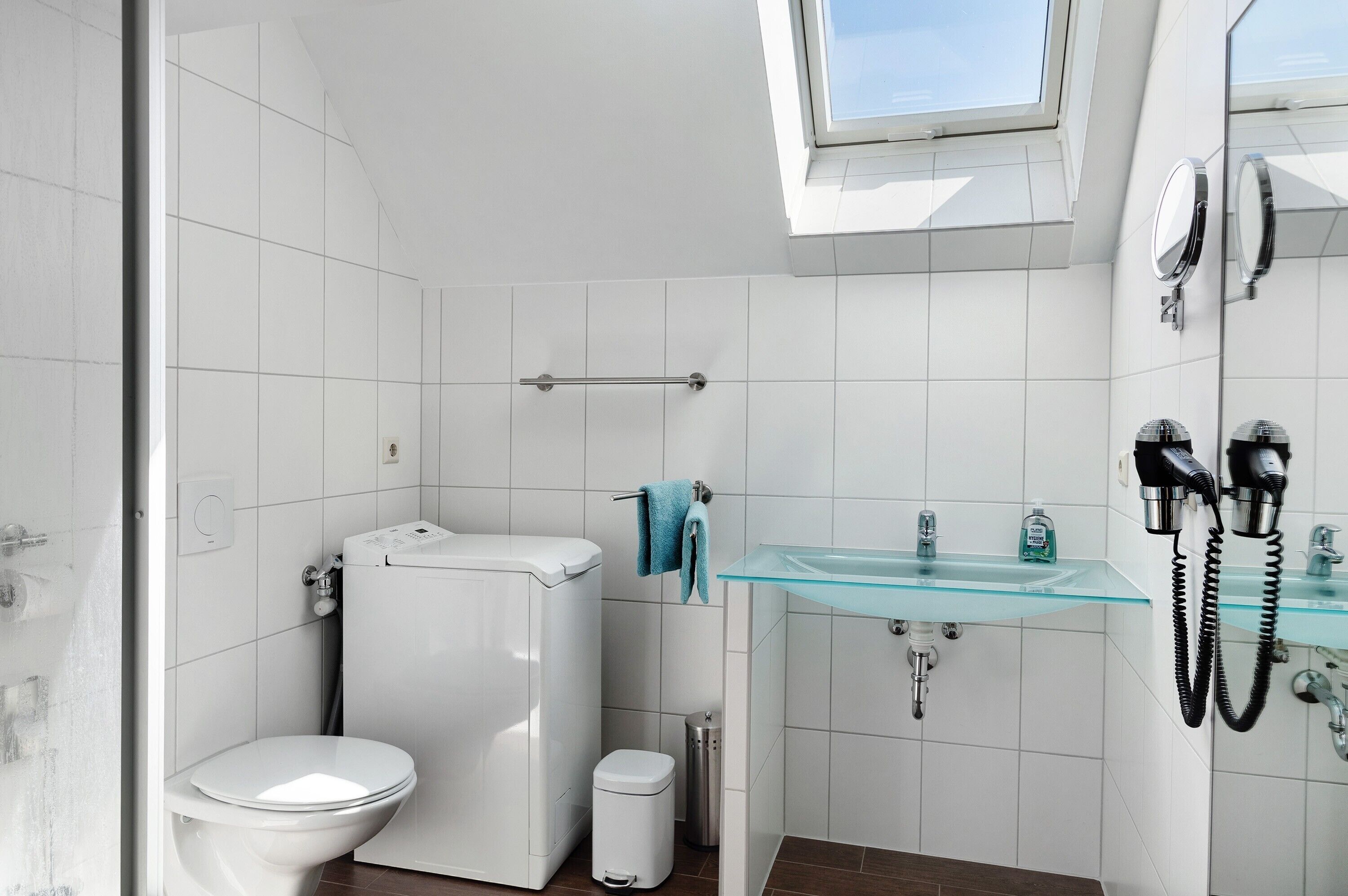 A modern bathroom with a toilet, bidet, glass sink, and a skylight.