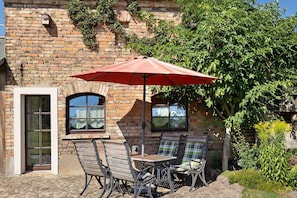 A brick building with a patio area featuring a table and two chairs, an umbrella, and a door.