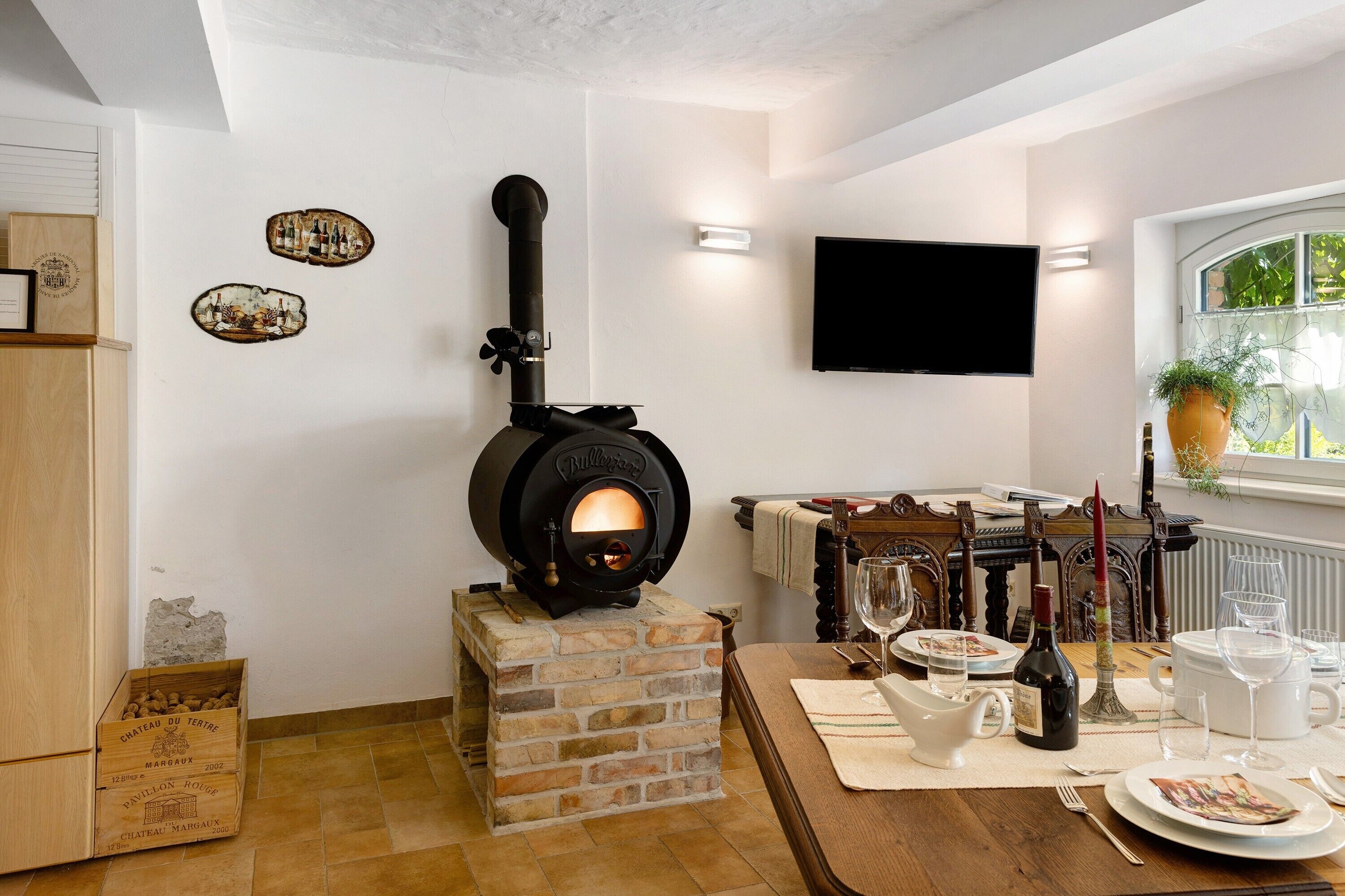 A room with a stone fireplace, a television mounted on the wall, and a dining table set for four.