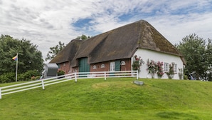 A traditional thatched-roof house with a white exterior, a white fence, and a grassy hill.