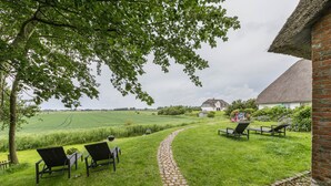 A grassy outdoor area with a cobblestone path, two lawn chairs, and a brick building with a thatched roof.