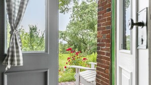 Blick durch eine Tür mit einem Karomuster-Vorhang, einer Ziegelwand und einer weißen Bank draußen.