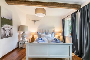 Une chambre à coucher comprenant un lit, des lampes de chevet, une lampe fixée au mur, une tête de lit, une fenêtre avec des rideaux et un tableau accroché au mur.
