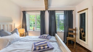 Ein Schlafzimmer mit zwei Betten, einem Holzstuhl, einem Nachttisch mit Lampe und einem Fenster mit Vorhängen.