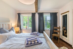 Une chambre avec deux lits, une chaise en bois, une table de chevet avec une lampe et une fenêtre avec des rideaux.
