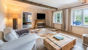 Ein Wohnzimmer mit einer Couch, einem Couchtisch, einem Fernseher und einem großen Fenster mit Vorhängen.