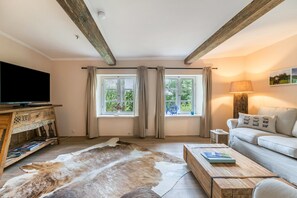 Un salon comprenant une télévision, un canapé, une table basse, des fenêtres avec des rideaux et un plafond en bois.