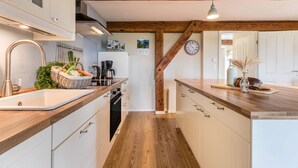 A kitchen with wooden beams, white cabinets, a sink, and a clock on the wall.