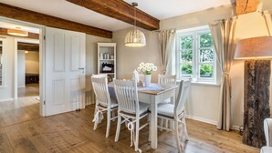 A dining area with a wooden ceiling, white chairs, a table, and a hanging light fixture.