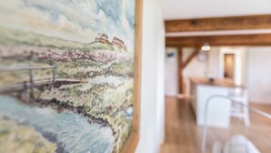 A room with a large painting of a landscape, wooden beams, a white chair, and a table.