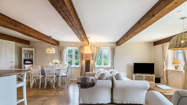 A spacious room with a wooden ceiling, a sofa set, a dining area, and a television.