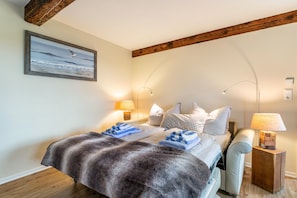 Une chambre à coucher avec un lit, deux tables de chevet, une lampe, un tableau et des poutres en bois au plafond.