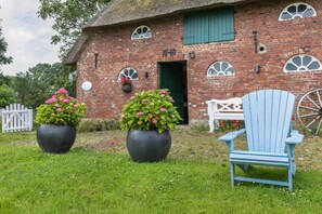 Un bâtiment en briques avec une porte verte, deux grands pots de fleurs et une chaise bleue.