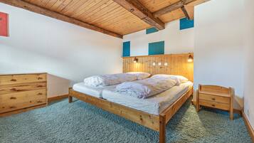 Quarto com cama de madeira, mesa de cabeceira, cômoda e teto com vigas aparentes.