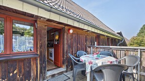 A wooden deck with a table and chairs, a red door, and a view of the interior.