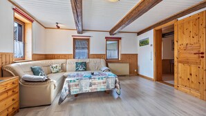 A room with a sofa, a table with a patterned tablecloth, wooden beams on the ceiling, and a wooden door.