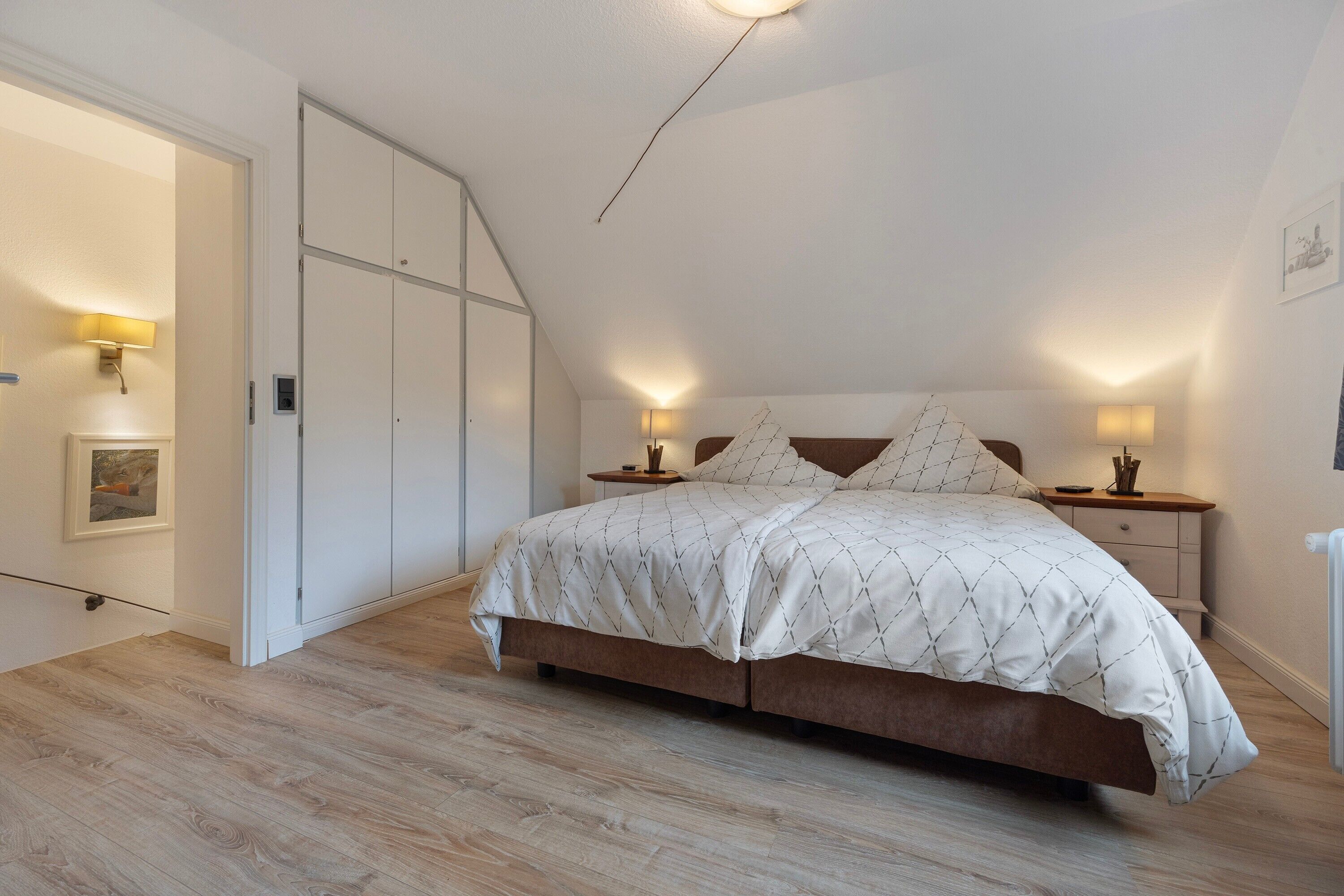 A bedroom with a bed, bedside tables, a lamp, a picture on the wall, and a door.
